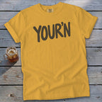 Yellow t-shirt with brown text reading "YOUR'N" and a glass of iced beverage.