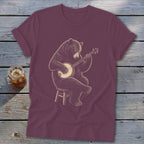 Bear playing a banjo while sitting on a stool, featured on a maroon t-shirt.
