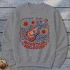 A gray crewneck sweatshirt features a folk art guitar graphic surrounded by sunflowers and the text "MOUNTAIN MELODIES".