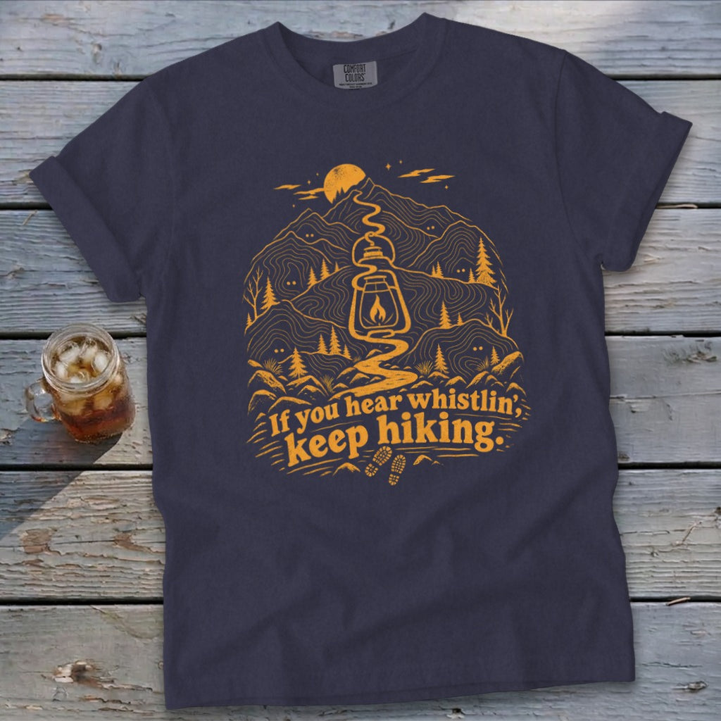 Navy t-shirt with orange graphic of a lantern, mountains, trees, and text "If you hear whistlin', keep hiking."