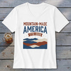 A white V-neck t-shirt featuring Mountain-Made America 1776-2026 graphic with mountains, stars, and stripes.