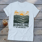 White t-shirt with "RIDGELINE AT DAYBREAK" graphic of a sunrise over mountains.