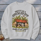 Speckled dog sleeps under red wagon with text "Pretty as a speckled pup".
