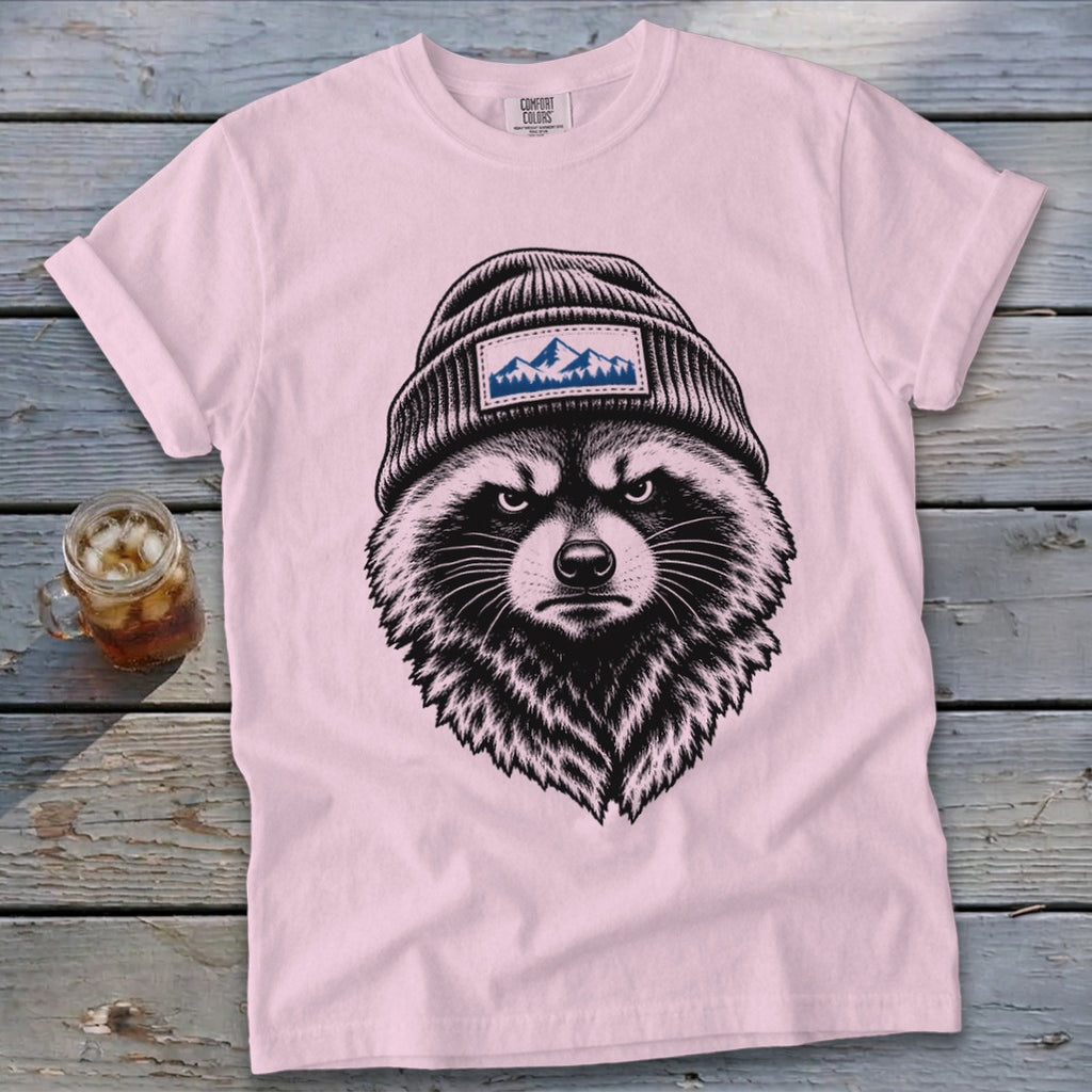 Pink t-shirt with a black ink drawing of a raccoon wearing a beanie with mountains.