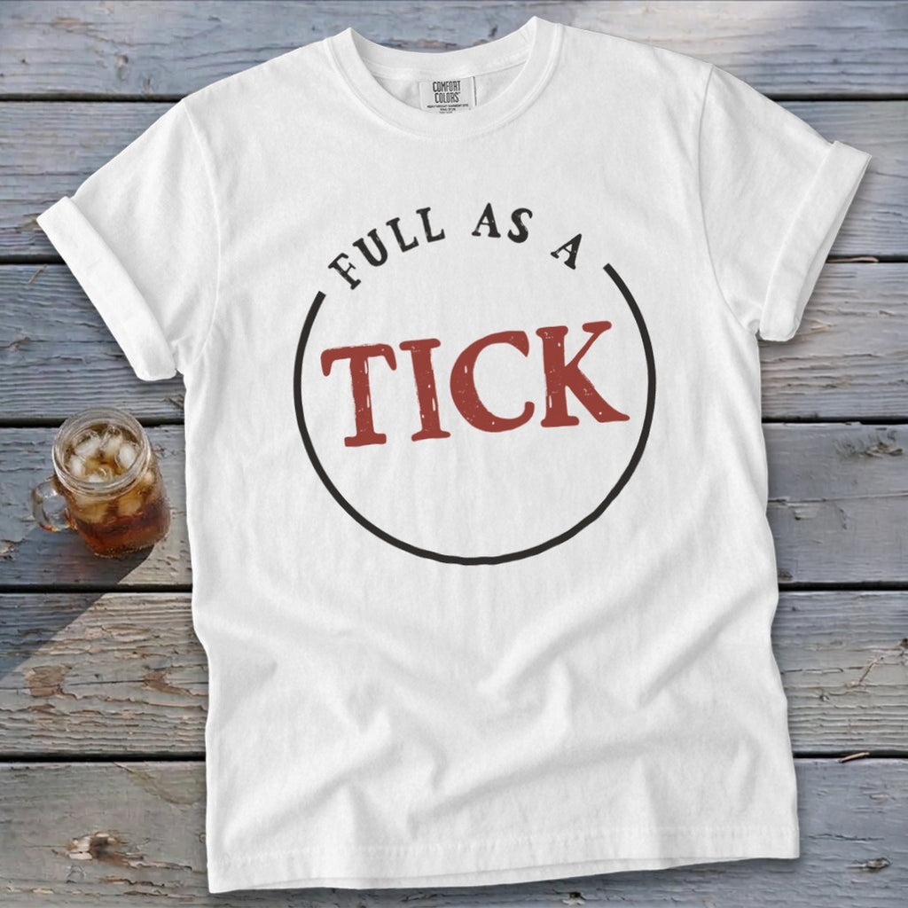 White t-shirt with "FULL AS A TICK" text design on a wooden surface.