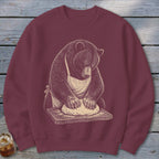 Bear wearing apron kneading dough on wooden board graphic on maroon sweatshirt.