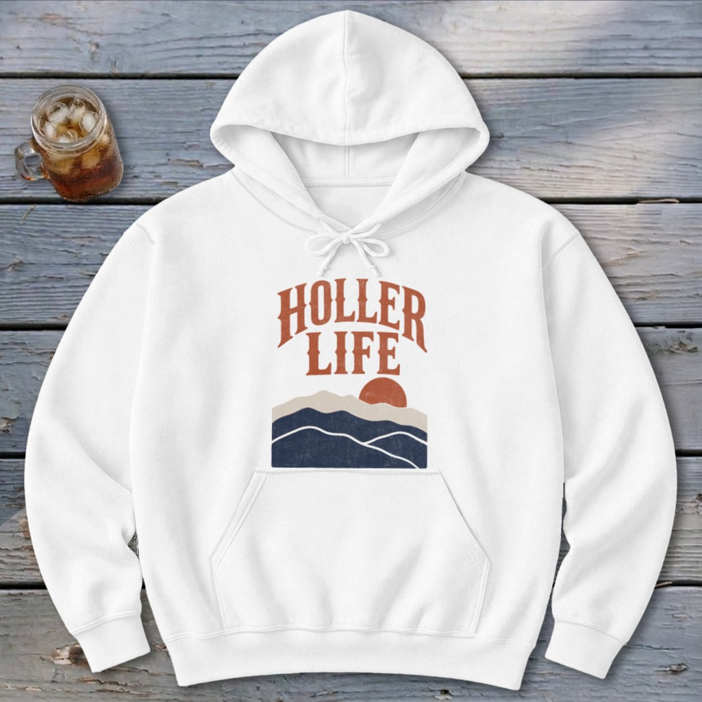 White hooded sweatshirt featuring retro graphic of mountains and the text Holler Life on wooden surface.
