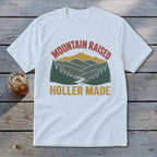 White t-shirt featuring a retro mountain graphic with the text Mountain Raised Holler Made.