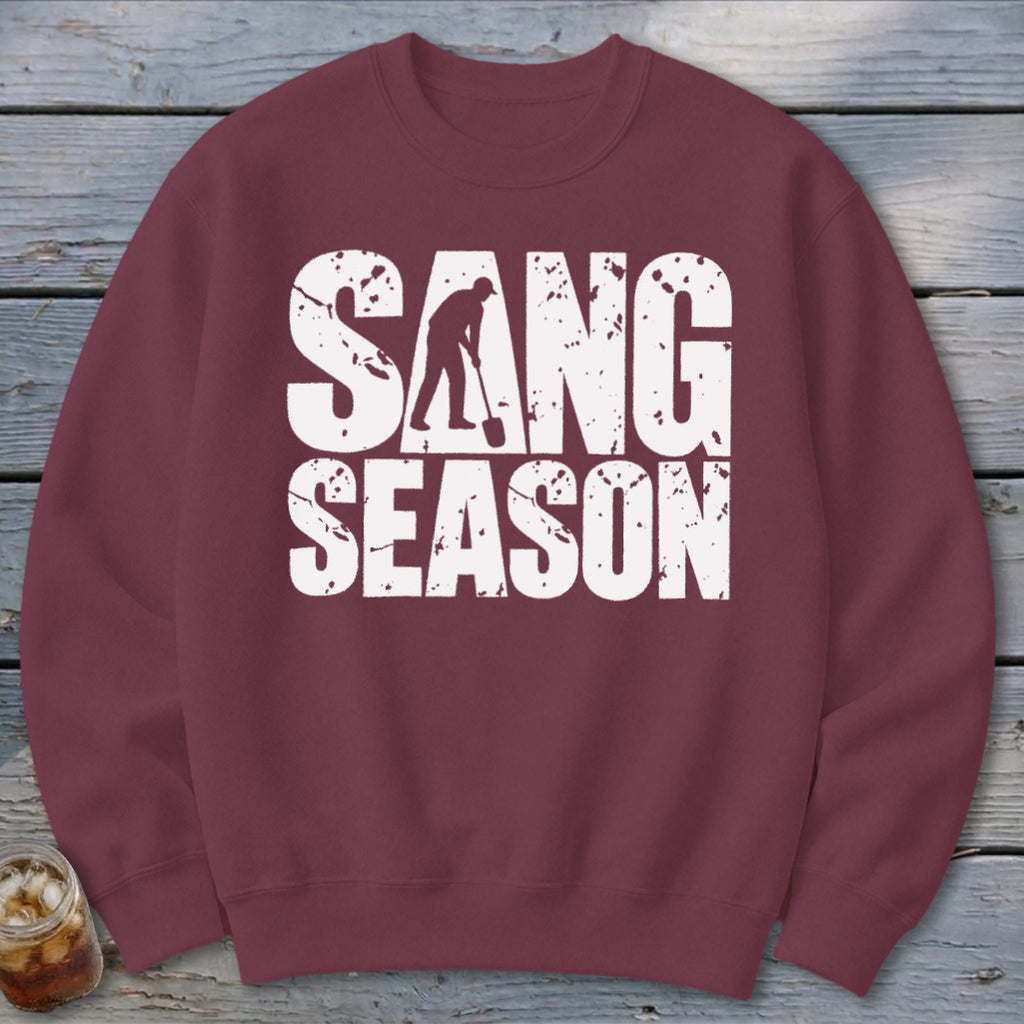 Maroon crewneck sweatshirt featuring white distressed text reading "SANG SEASON" with a person digging.