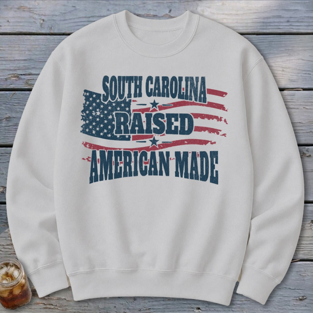 White sweatshirt with "South Carolina Raised American Made" text and distressed American flag graphic.