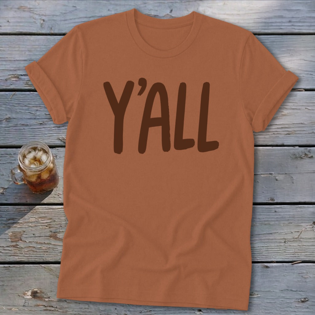 Brown t-shirt with "Y'ALL" text in dark brown, on a wooden surface.