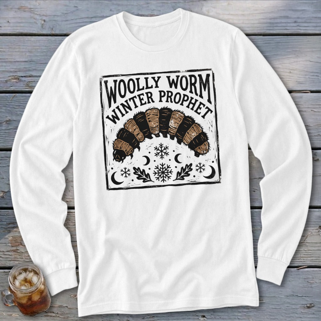 A white long-sleeved shirt features a black and brown graphic of a woolly worm with snowflakes, crescent moons, and text reading Woolly Worm Winter Prophet.