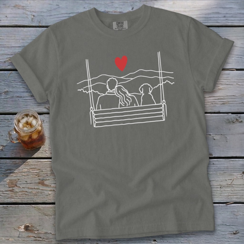 Gray t-shirt with line art of couple and dog on a swing, red heart above.