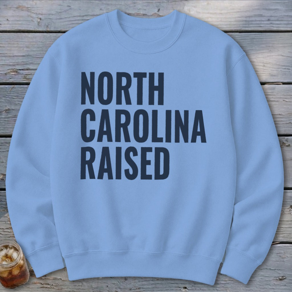 Light blue sweatshirt with "North Carolina Raised" in dark blue text.