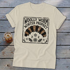 A cream-colored t-shirt features a black block-print graphic of a woolly worm, snowflakes, and the text "Woolly Worm Winter Prophet."