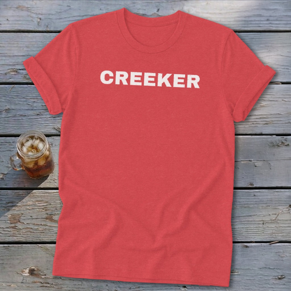 Red t-shirt with "CREEKER" printed in white text, next to a glass of iced tea.