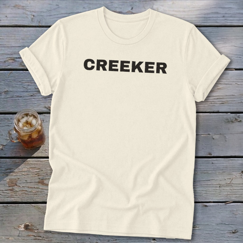 Cream t-shirt with "CREEKER" text in black, next to a glass of iced beverage.