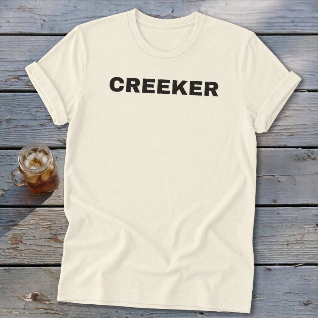 Cream t-shirt with "CREEKER" text in black, next to a glass of iced beverage.