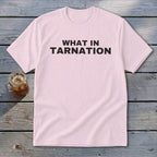 Pink t-shirt with black text "WHAT IN TARNATION" next to a glass of iced tea.