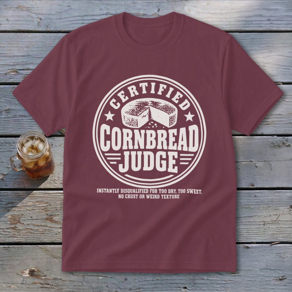 Maroon short-sleeved t-shirt featuring a white round graphic with a cornbread illustration and text.