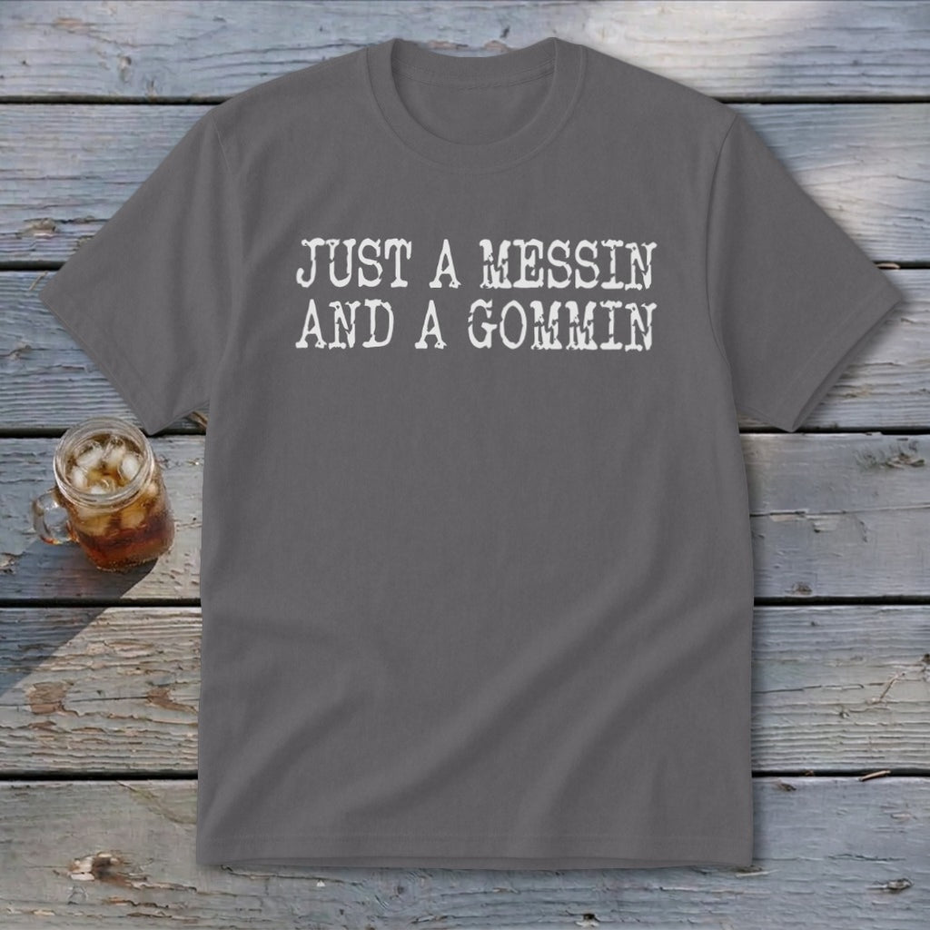 Gray t-shirt with white text "JUST A MESSIN AND A GOMMIN" and a glass of iced tea.