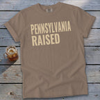 T-shirt with "PENNSYLVANIA RAISED" text in cream on a brown background.