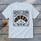 A white t-shirt featuring a graphic of a woolly worm caterpillar, snowflakes, and the text Woolly Worm Winter Prophet.