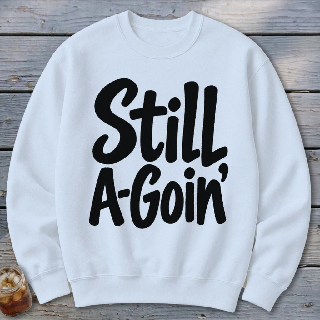 White crewneck sweatshirt featuring bold black text on the chest that reads Still A-Goin'.