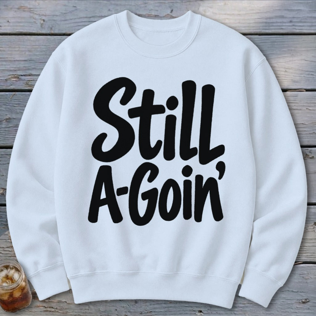 White crewneck sweatshirt featuring bold black text on the chest that reads Still A-Goin'.