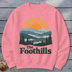 Pink sweatshirt with a sunset over mountains and the text "The Foothills."