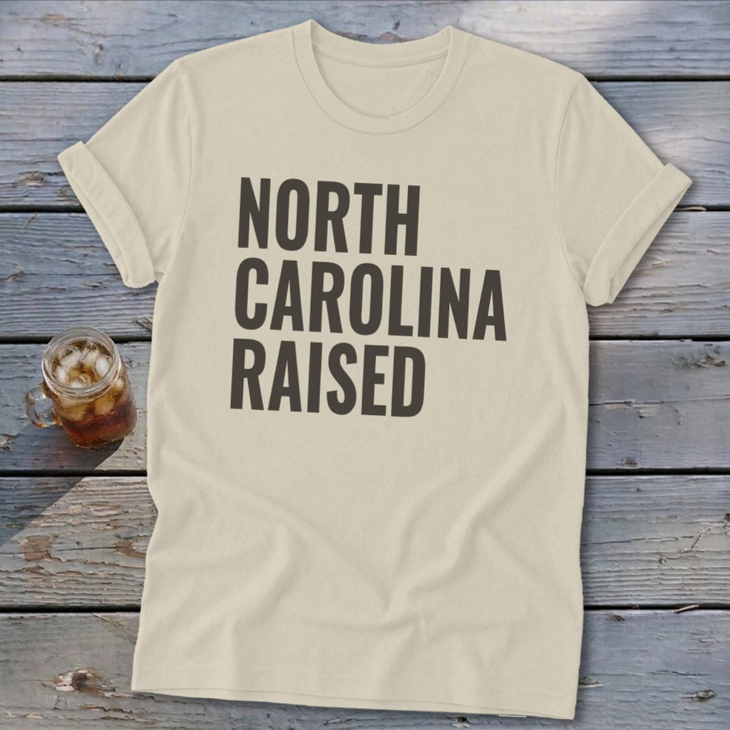 Cream t-shirt with bold black text reading "NORTH CAROLINA RAISED."