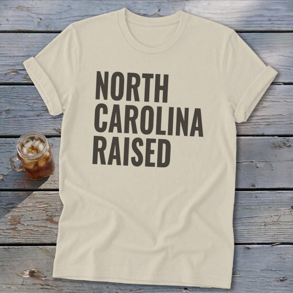 Cream t-shirt with bold black text reading "NORTH CAROLINA RAISED."