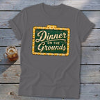 A dark gray t-shirt featuring a green vintage-style sign graphic that reads Dinner on the Grounds.