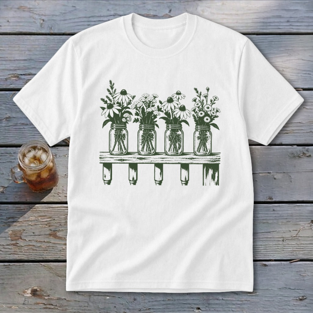 White t-shirt featuring a green botanical illustration of four mason jars filled with wildflowers on a shelf.