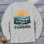 White long sleeve shirt with a mountain and sun graphic and "The Foothills" text.