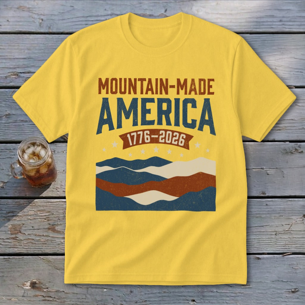 Yellow crewneck t-shirt with Mountain-Made America and 1776-2026 text above a patriotic mountain graphic.