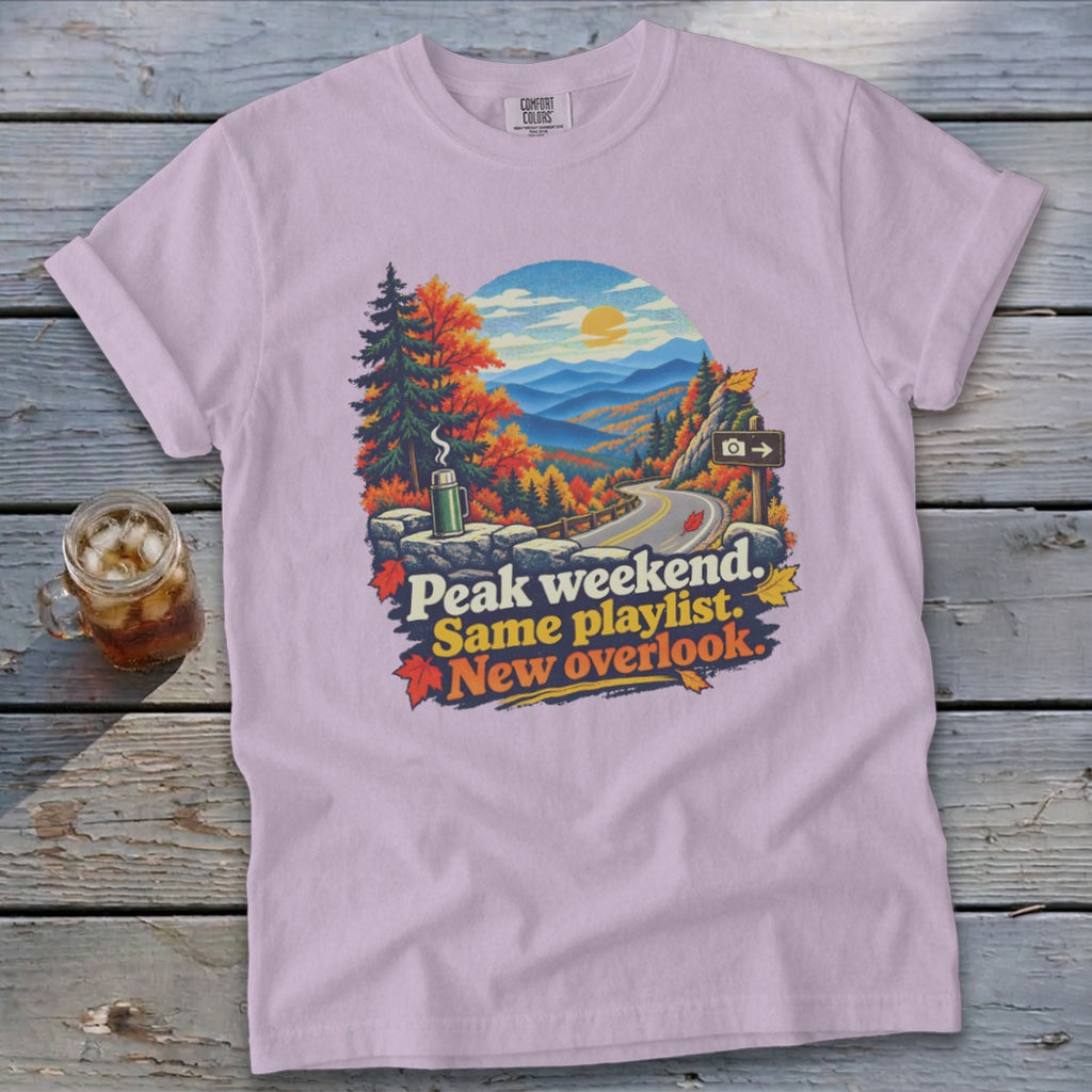 Lilac t-shirt with mountain overlook graphic and text "Peak weekend. Same playlist. New overlook."