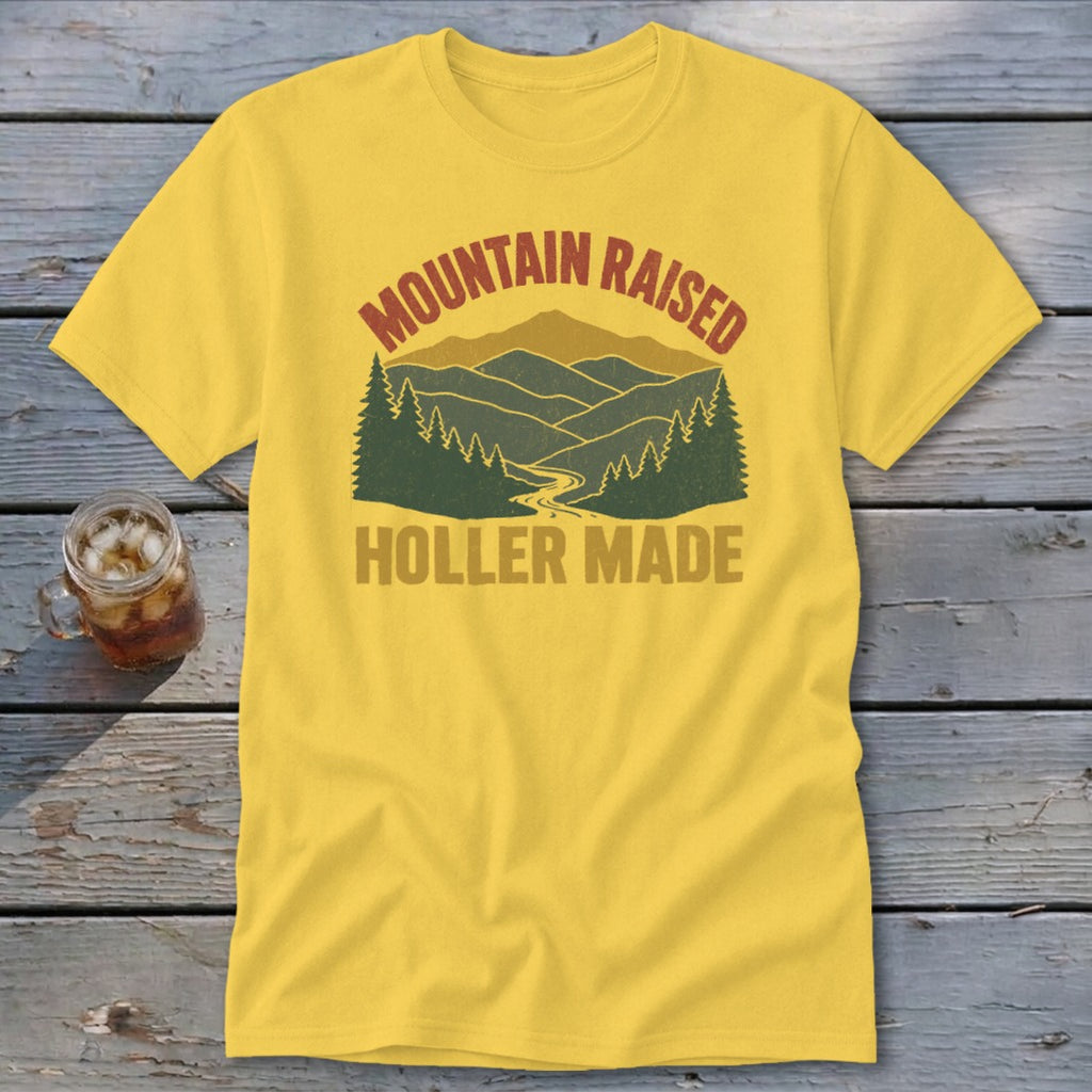 A yellow t-shirt with a vintage graphic of mountains, trees, and the text "MOUNTAIN RAISED HOLLER MADE."
