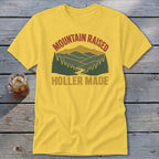 A yellow t-shirt with a vintage graphic of mountains, trees, and the text "MOUNTAIN RAISED HOLLER MADE."