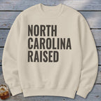 Cream sweatshirt with black text reading "NORTH CAROLINA RAISED".