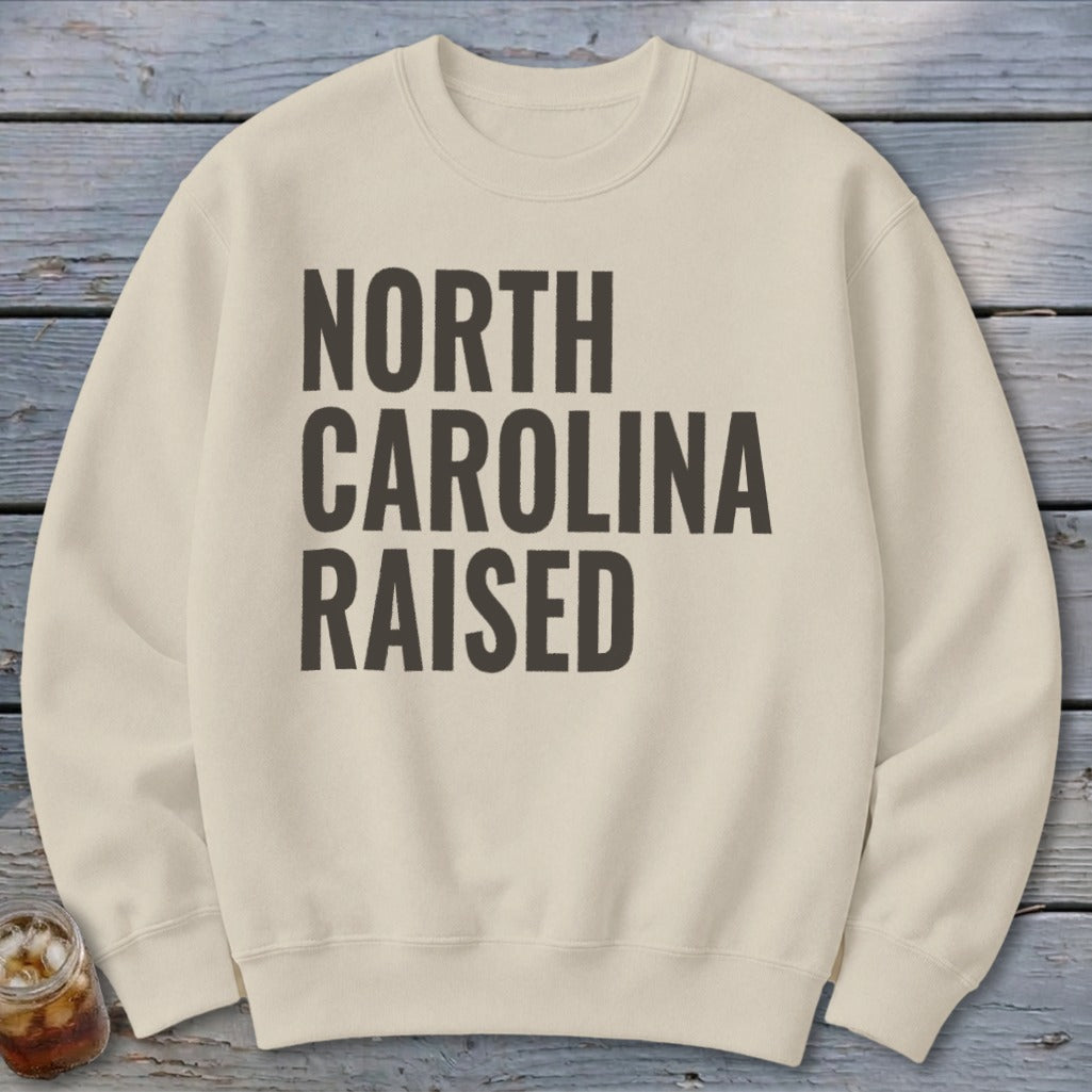 Cream sweatshirt with black text reading "NORTH CAROLINA RAISED".
