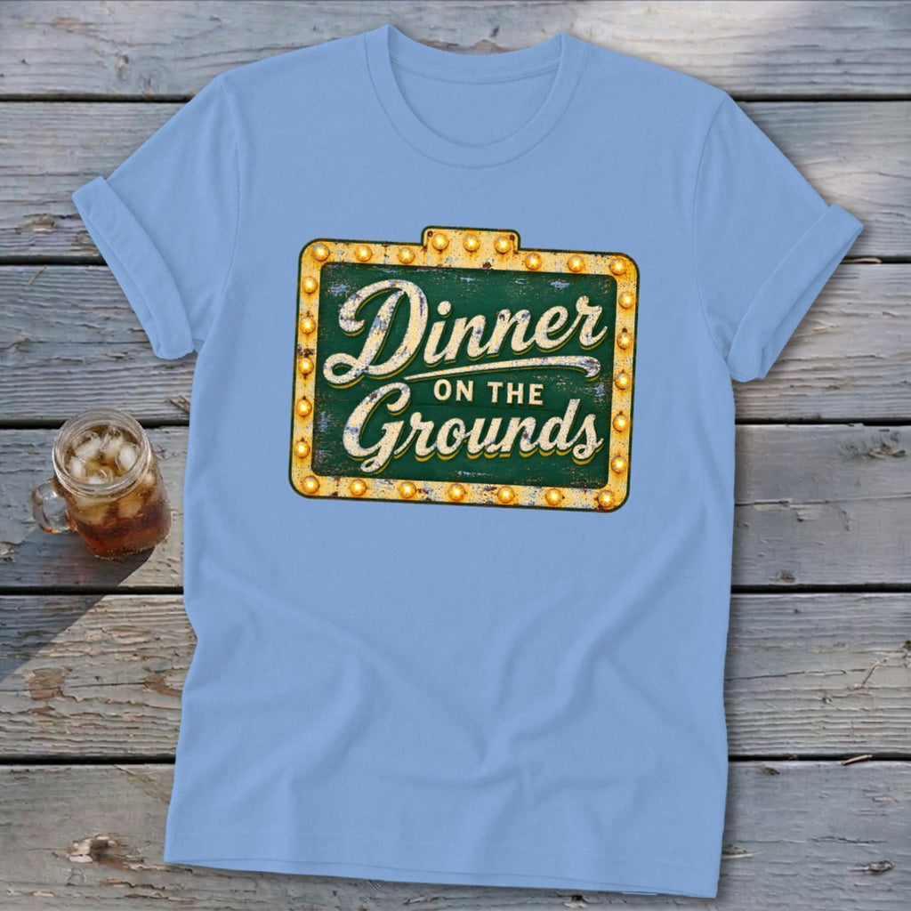 Light blue t-shirt featuring a green sign graphic with Dinner on the Grounds text.