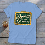 Light blue t-shirt featuring a green sign graphic with Dinner on the Grounds text.