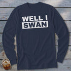 Dark blue long-sleeve t-shirt with white block text reading WELL I SWAN on a wooden background.