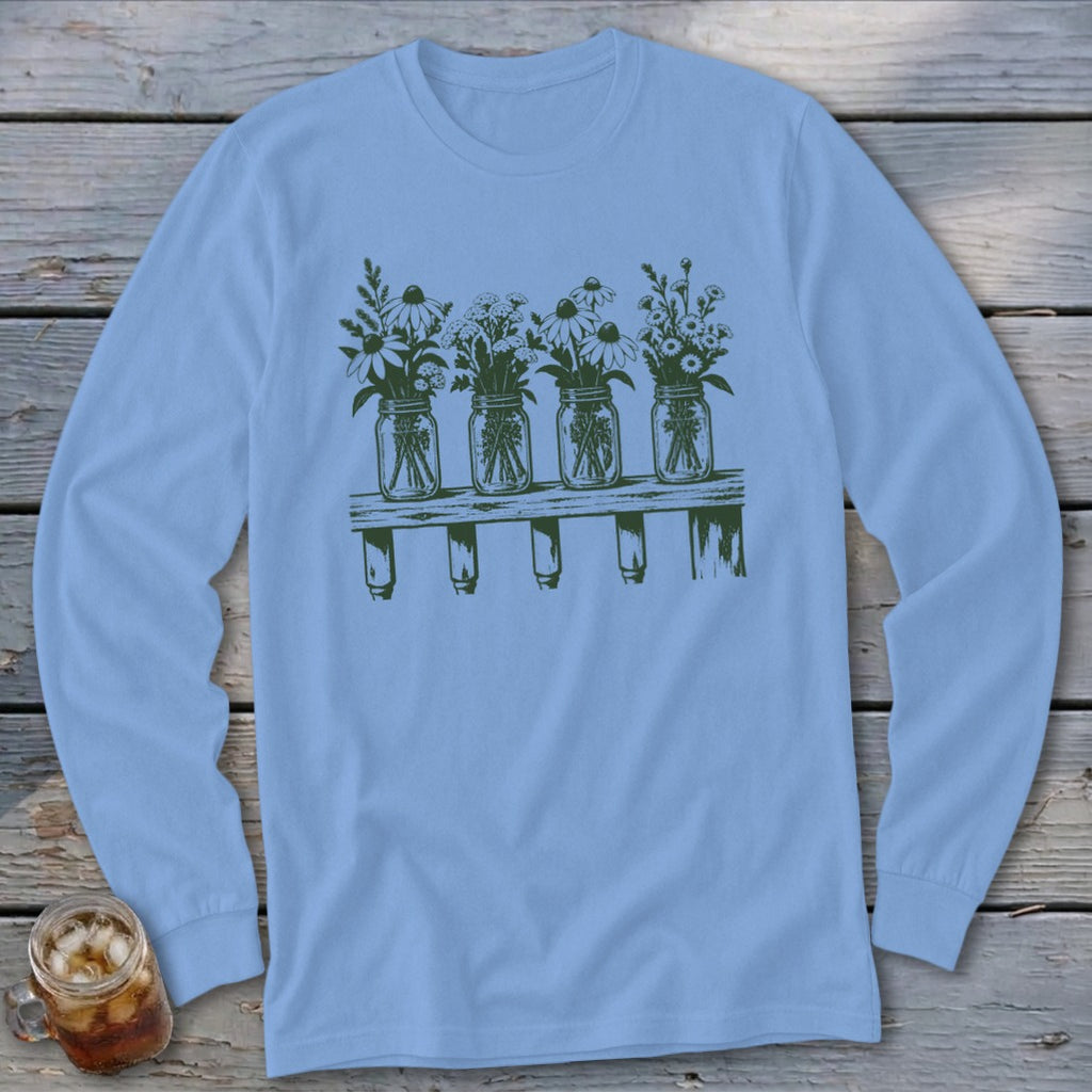 A light blue long-sleeve t-shirt featuring a green graphic of four mason jars filled with wildflowers on a wooden shelf.