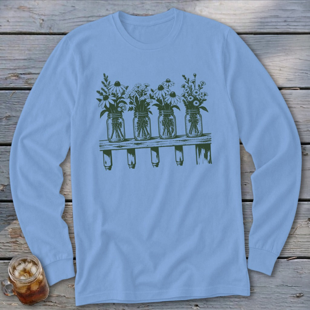 A light blue long-sleeve t-shirt featuring a green graphic of four mason jars filled with wildflowers on a wooden shelf.