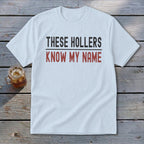 White t-shirt with "THESE HOLLERS KNOW MY NAME" printed in black and red text.