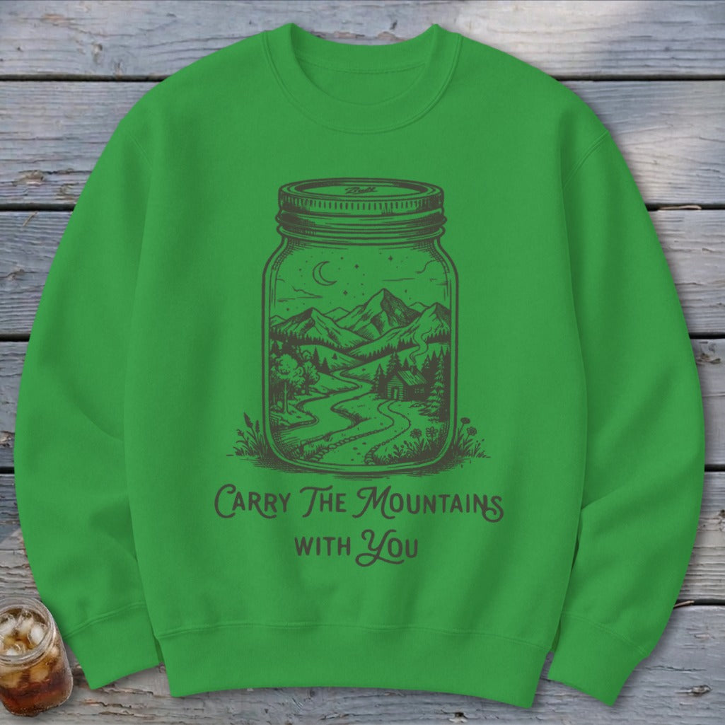 Green crewneck sweatshirt featuring a black graphic of a mountain landscape inside a glass jar, with the text Carry The Mountains With You.