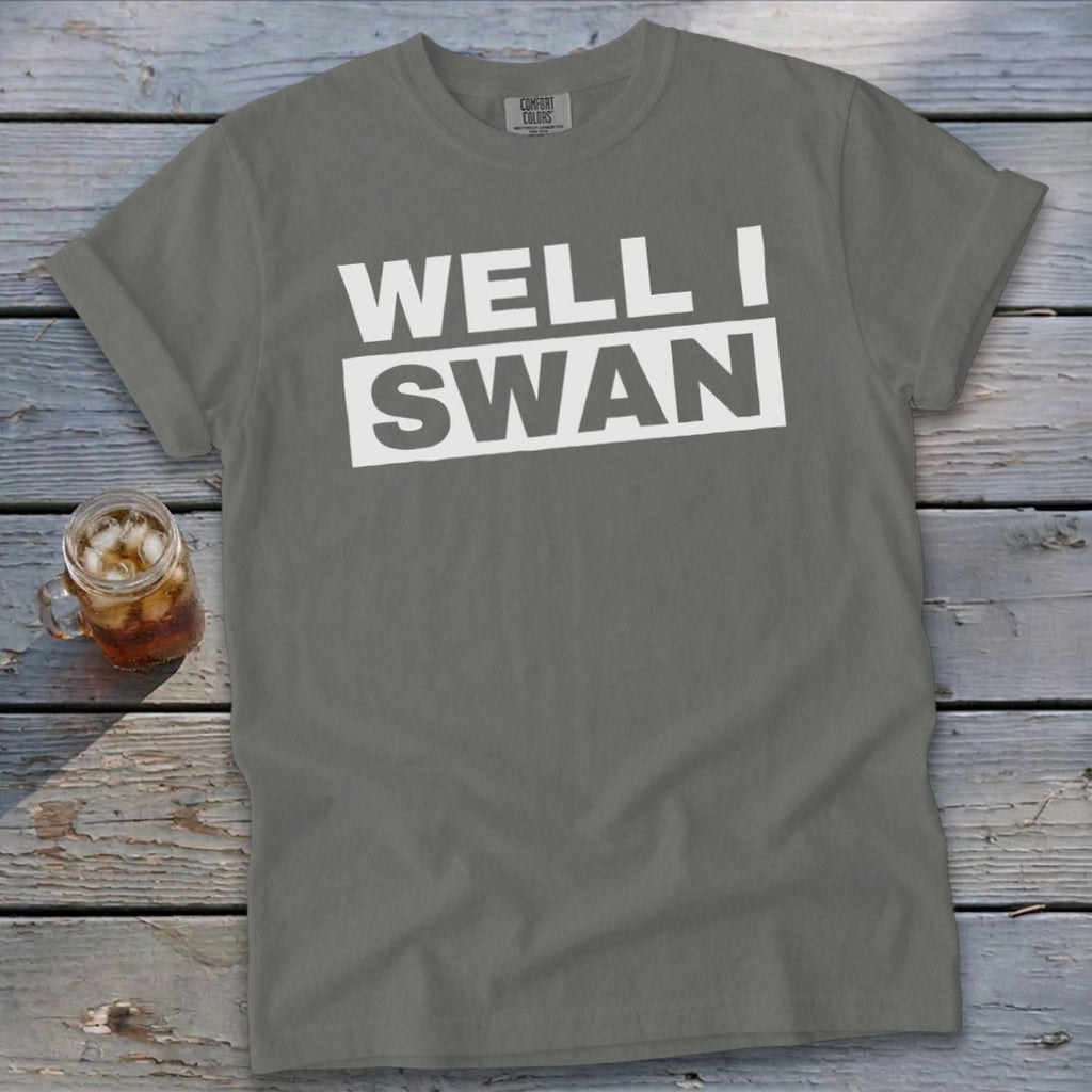 Grey t-shirt featuring the white text "WELL I SWAN" on a wooden background with a glass of iced tea.