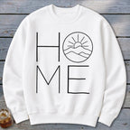 A white crewneck sweatshirt features black text spelling "HOME" with a mountain and sun graphic replacing the letter "O".